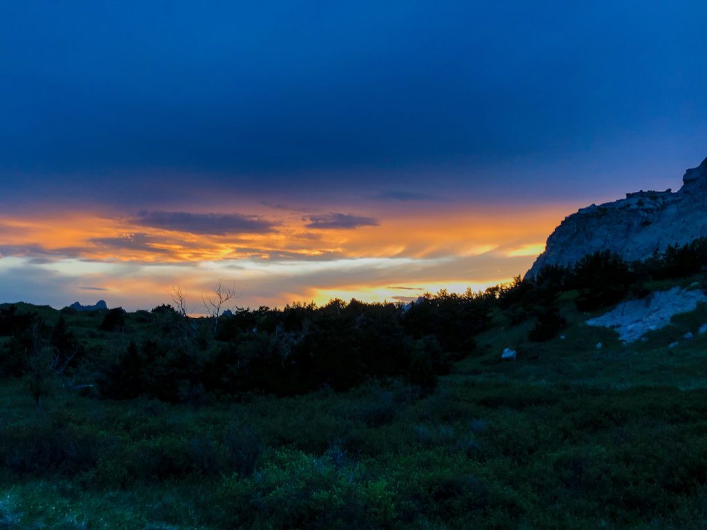 Sunrise is just above a dark ridge line illuminating the clouds with a yellow-orange glow that fades to a dark blue at the top of the image